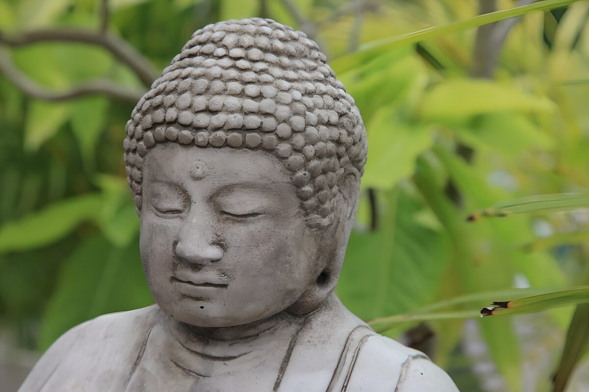 Graue Buddhafigur vor grünem Blätterwerk