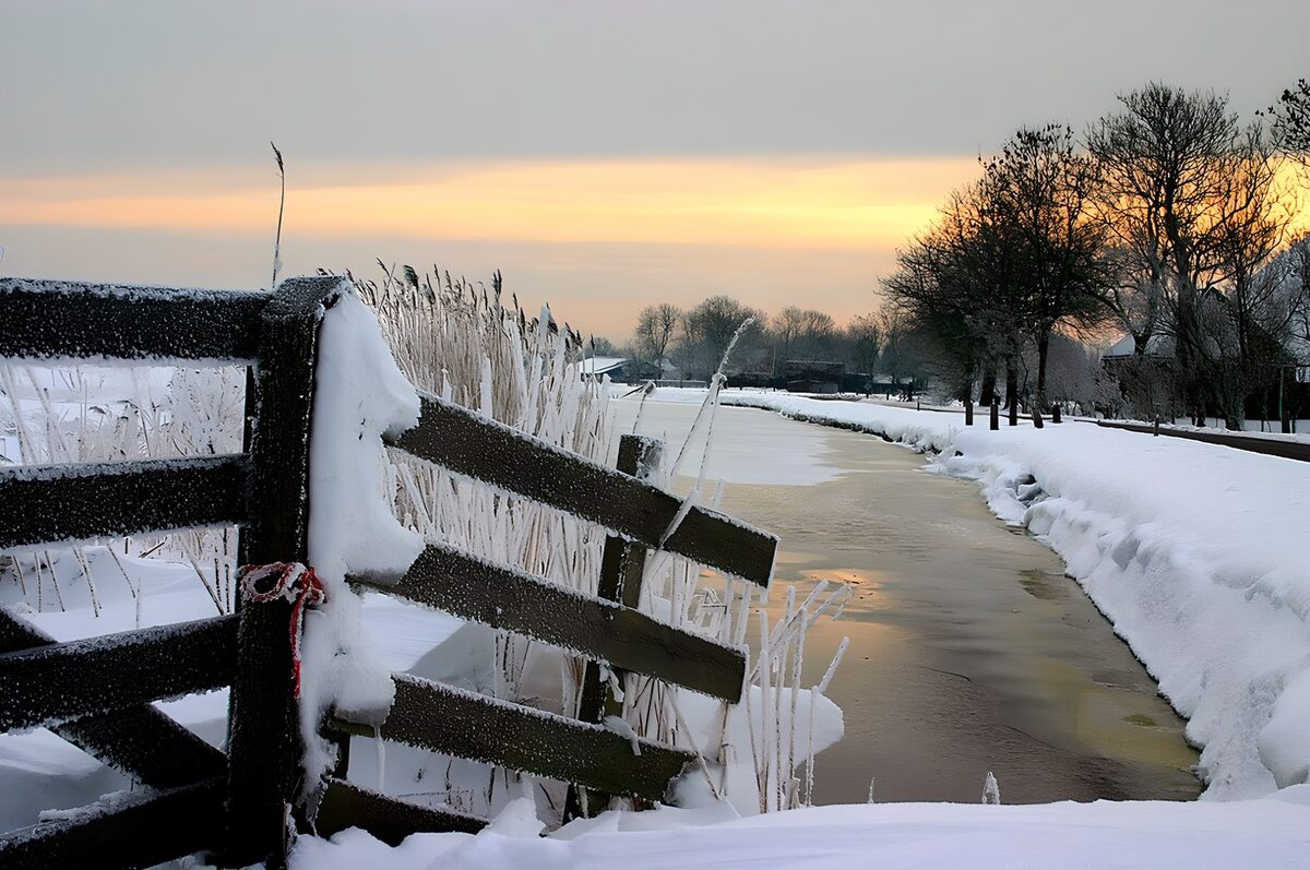 Verschneiter Zaun am Kanal im Abendlicht