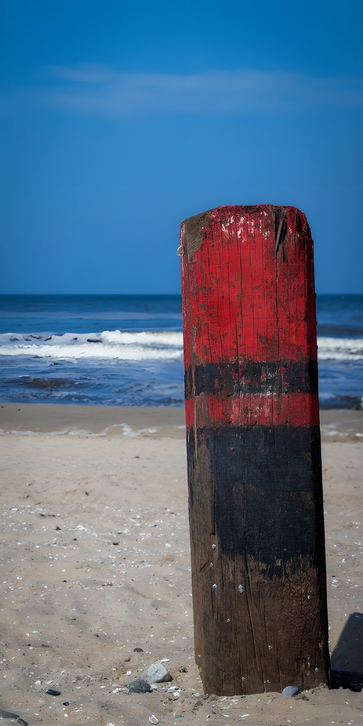 Verwitterter Strandpfosten in Rot und Schwarz