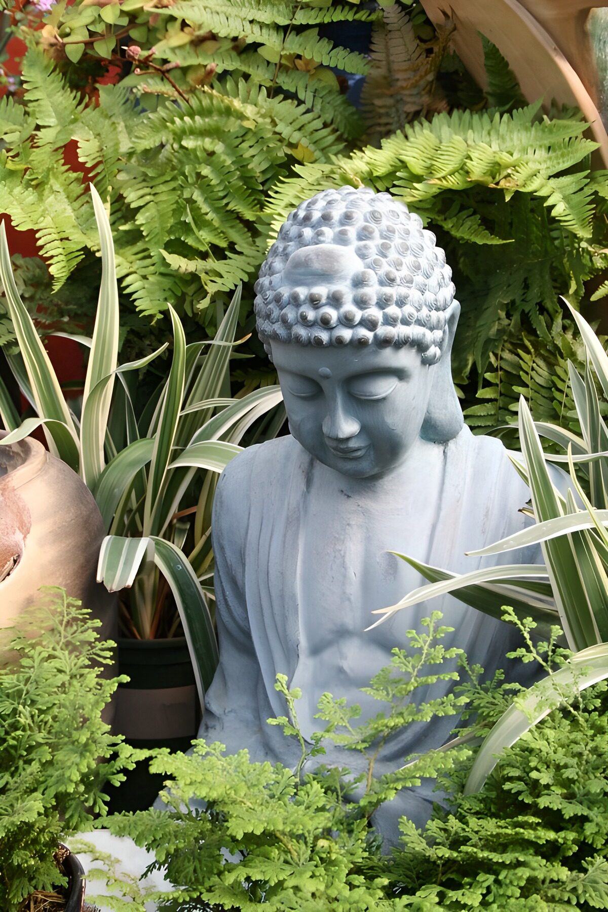 Grauer Buddha zwischen grünen Farnen