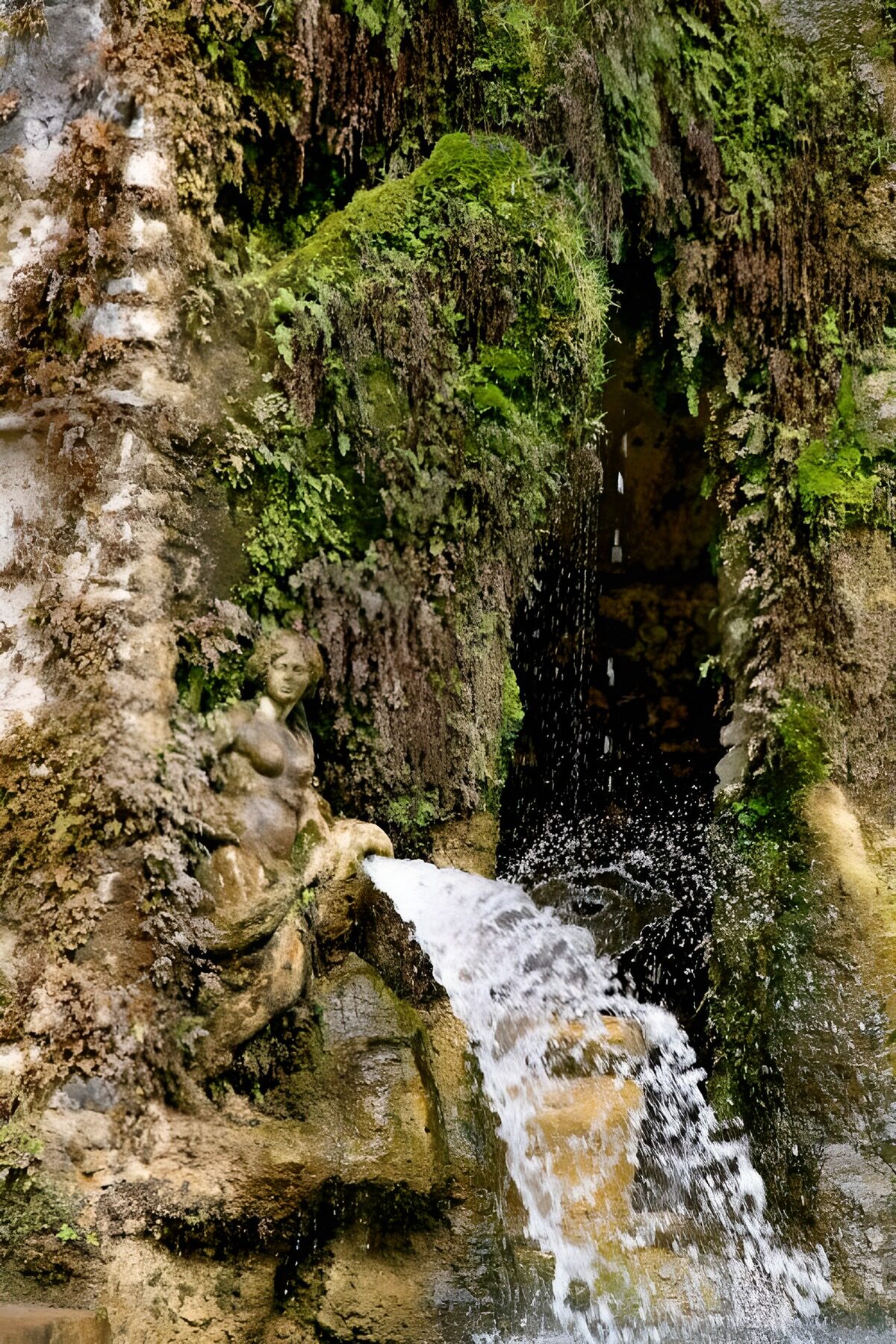 Steinbrunnen mit Frauenfigur im Moos