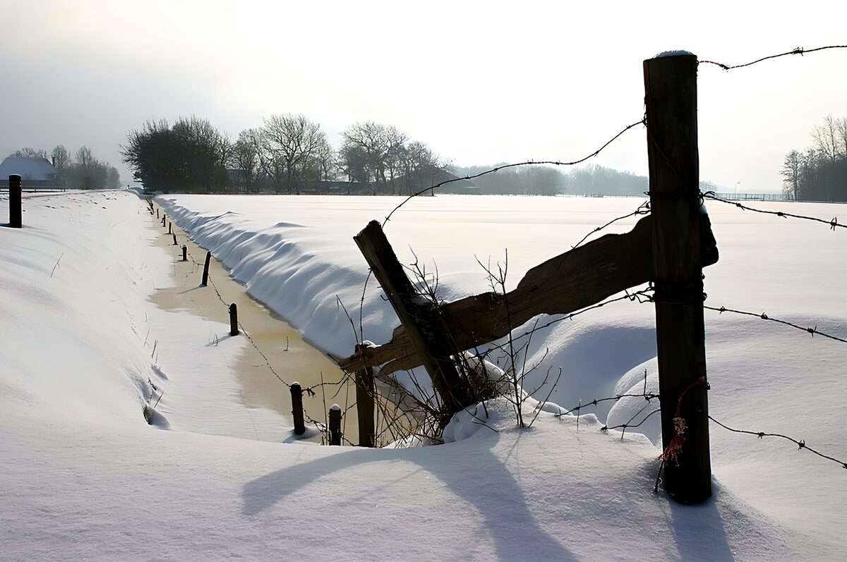 Vereister Graben mit Zaun im Schnee
