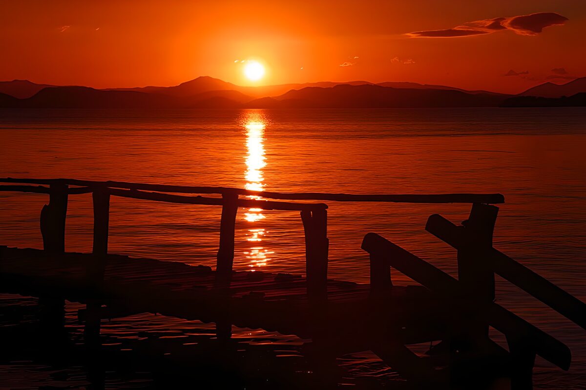 Sonnenuntergang am Steg vor dunklen Bergen