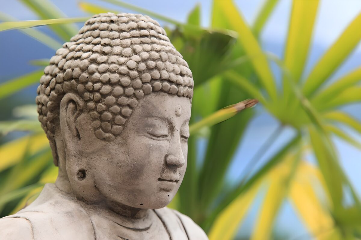Graue Buddha-Statue vor grünem Laub