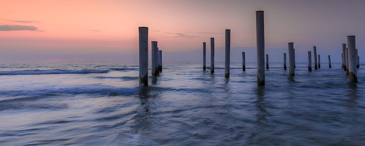 Pfähle im Meer bei rosa Abendlicht