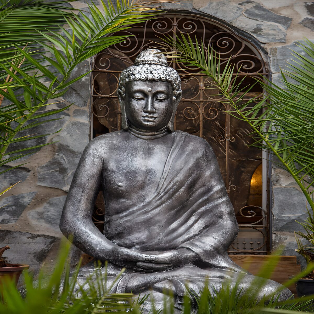 Silbergrauer Buddha zwischen Palmwedeln