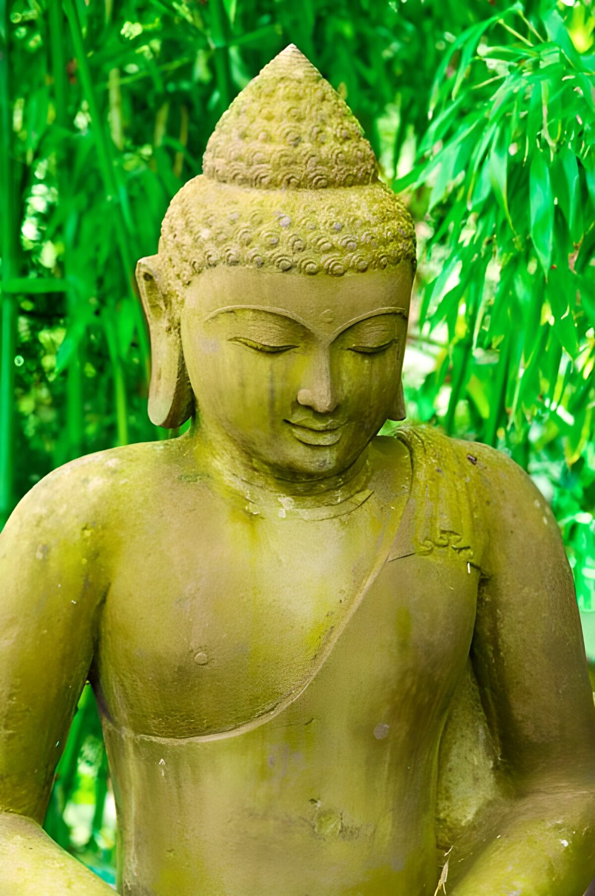 Verwitterte Buddhastatue vor grünem Bambus