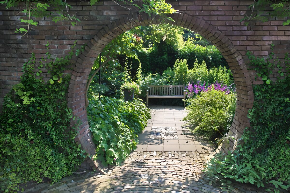 Gartenbank hinter bewachsenem Ziegelbogen