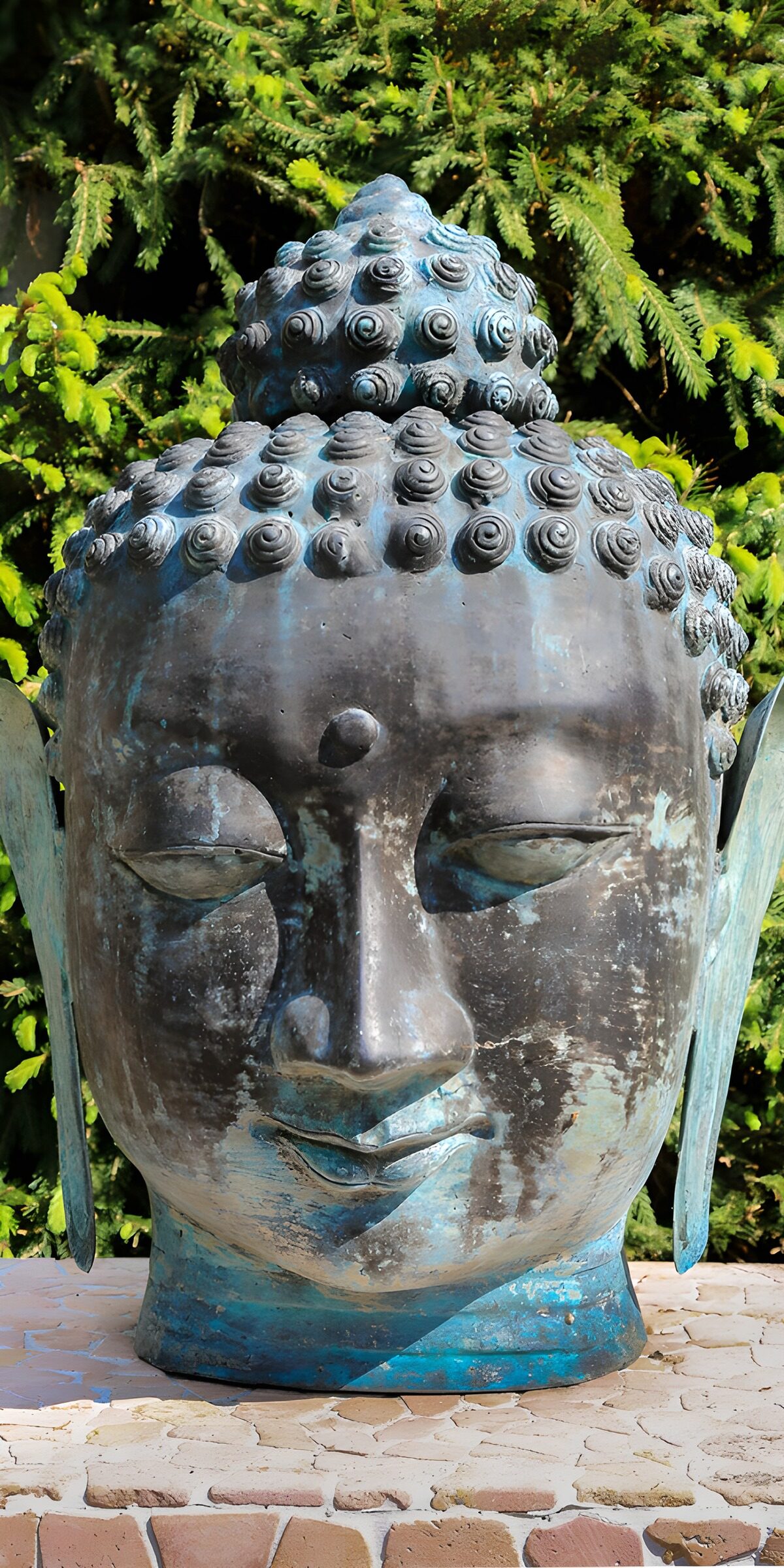 Buddhakopf mit blauer Patina im Grünen