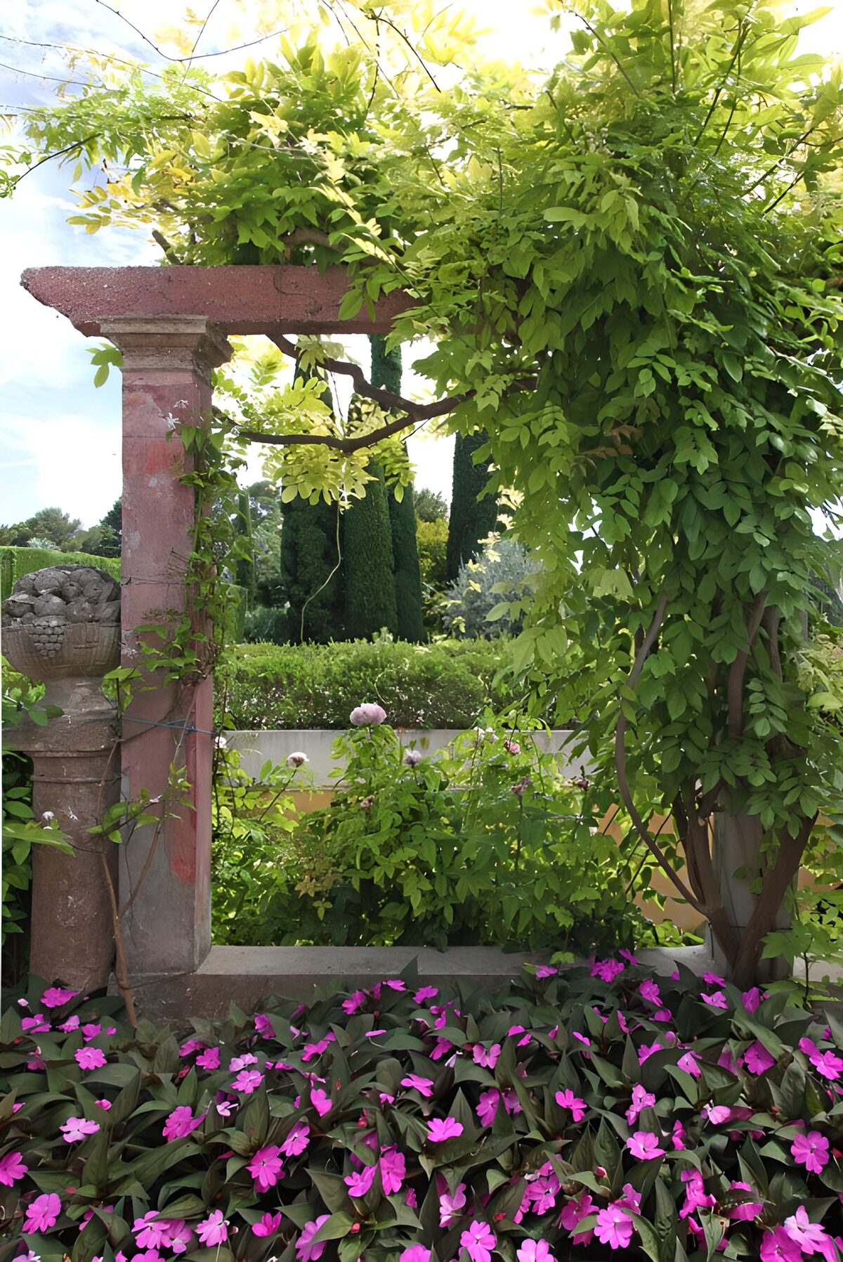 Steinpergola mit rosa Blüten im Sonnenlicht