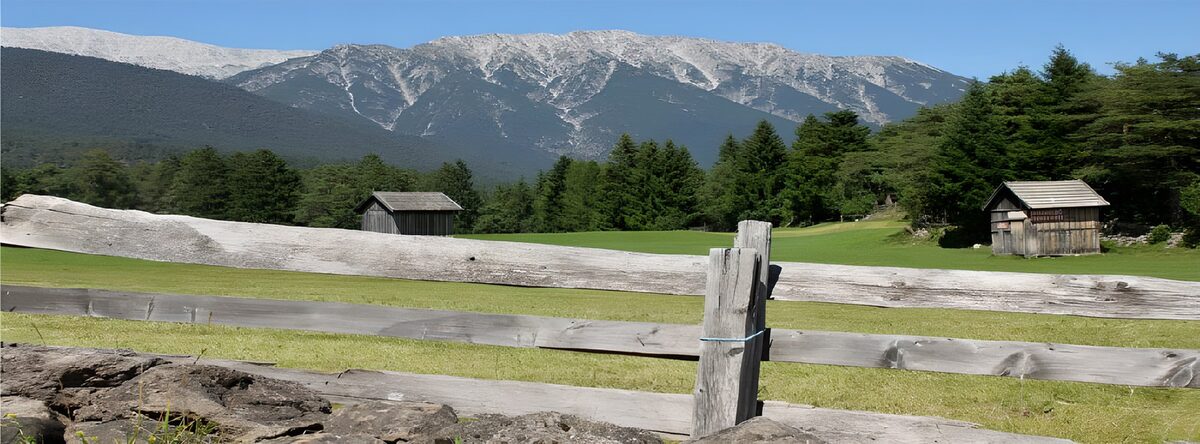 Sonnige Bergwiese mit Hütten und Holzzaun